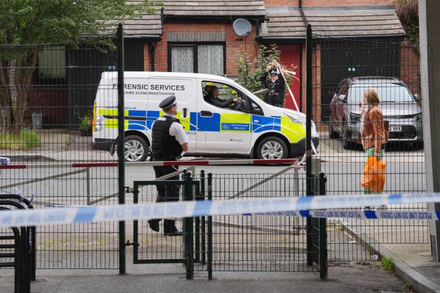 Police forensic services van parked on a road, there's a police man and a pedestrian. The photo is taken from behind a wired fence