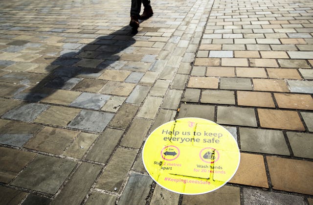 A person casts a shadow walking past a social distancing information sign painted on the pavement in Leeds city centre, some six months on from the evening of March 23, when Prime Minister Boris Johnson announced nationwide restrictions