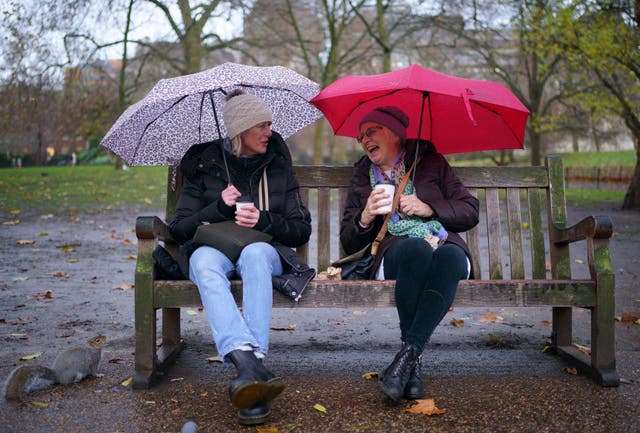 Two people are seen sitting on a bench with umbrellas