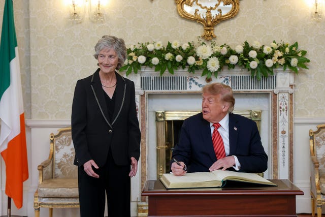 President Catherine Connolly stands by as US President Donald Trump signs the visitors' book at Áras an Uachtaráin, her official residence in Phoenix Park, Dublin 