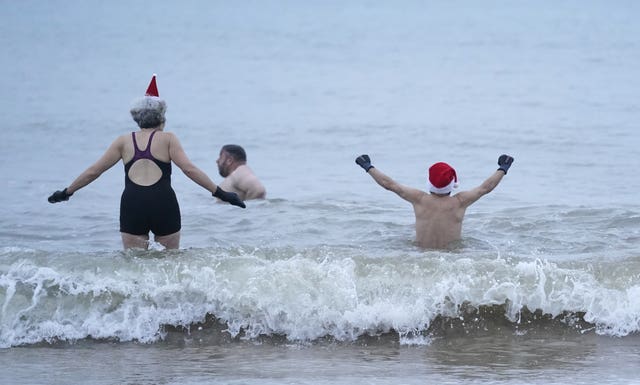 A man and woman in Santa hats walk into the waves