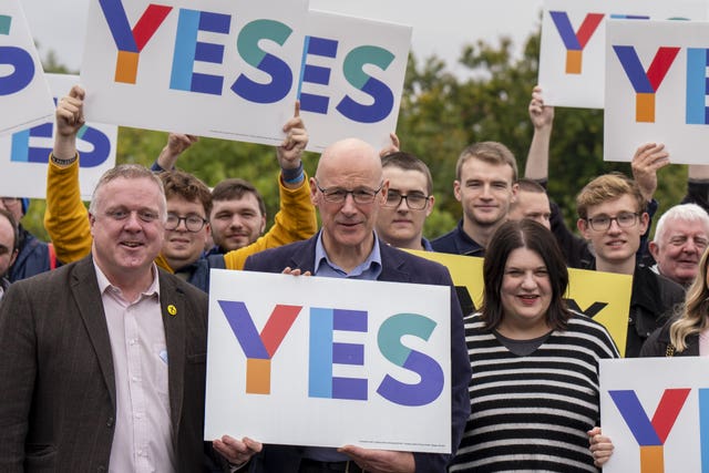 John Swinney holding Yes placards and standing among SNP supporters