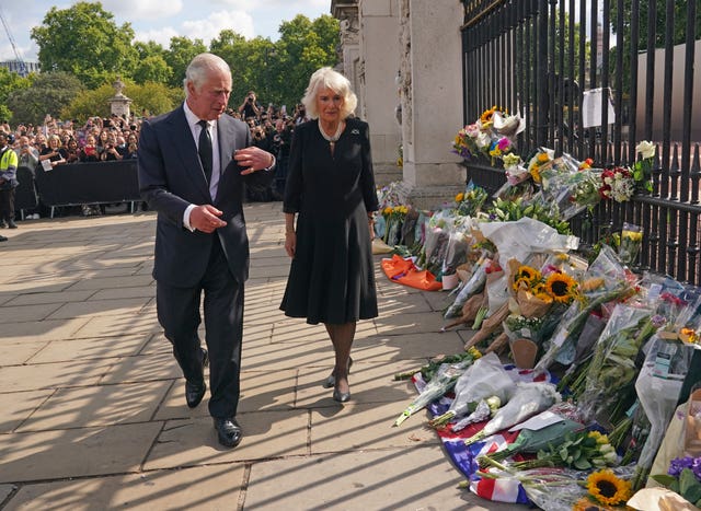 The King, with Queen, points at the collection of floral tributes left at the Buckingham Palace gates the day after Queen Elizabeth II's death