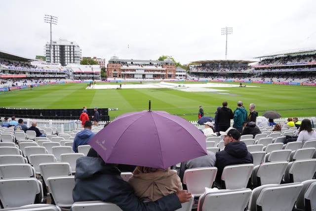 Covers are on as people shelter under a umbrella from rain on day three of the second Rothesay Test match at Lord’s in London