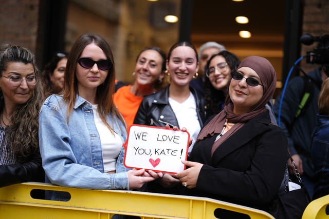 Two women hold a handwritten sign which says 'we love you Kate'