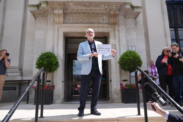 Jeremy Corbyn stands in front of Islington Town Call with a poster bearing his name and the word 