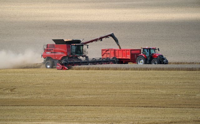 A tractor drives alongside a combine harvester (Andrew Matthews/PA)