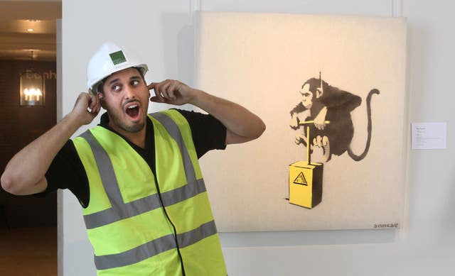 A workman in hi-vis jokes next to Banksy’s Monkey Detonator 