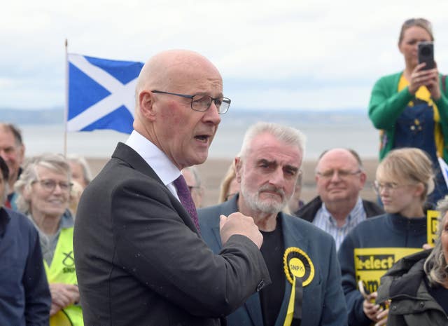 John Swinney speaking in a group of SNP supporters on a beach