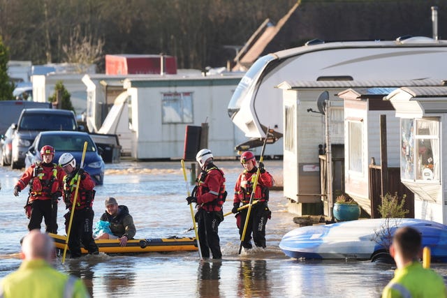 Rescuers help a man in a yellow rubber dinghy. There is flooding and caravans have been covered in water.