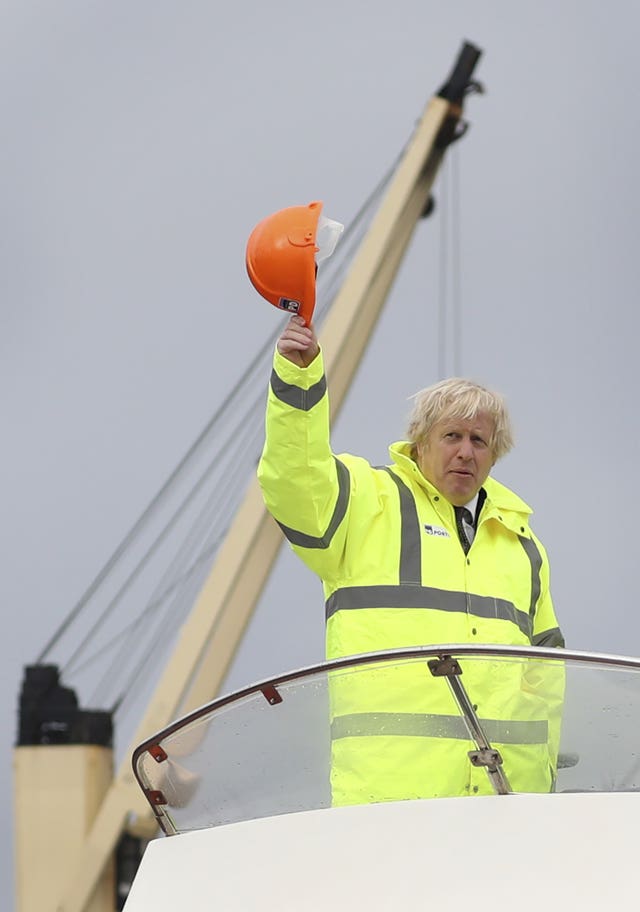 Prime Minister Boris Johnson waves his hard hat as he travels aboard a boat on the River Tees during a visit to Teesport in Middlesbrough (Scott Heppell/PA)