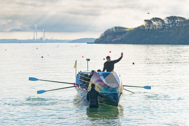A man waves while another pushes a rowing boat out into the sea