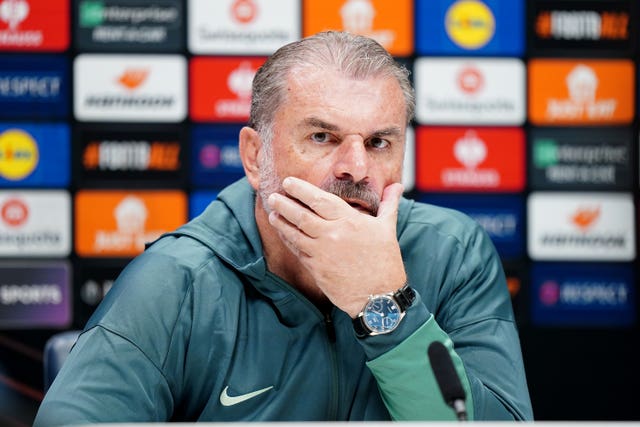 Tottenham manager Ange Postecoglou, with his left hand over his mouth, faces the media