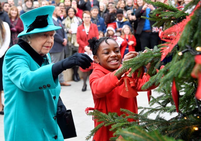 Queen Elizabeth II and Shylah Gordon-Clarke,  then 8, attach a bauble to a Christmas tree during her visit to Coram, the UK’s oldest children’s charity