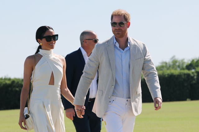 Harry and Meghan walk hand in hand in the sunshine wearing sunglasses at the polo