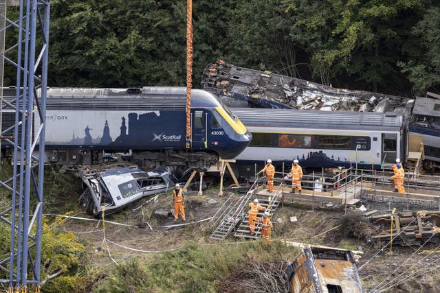 Workmen alongside derailed train as engine is lifted awaye