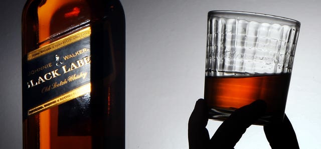A bottle of Johnnie Walker Black Label whisky and a hand holding a glass with liquid in it
