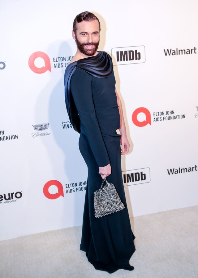 Jonathan Van Ness smiling while posing for photos in a green floor-length dress with metallic bag
