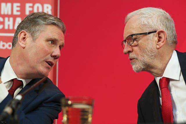 Keir Starmer and Jeremy Corbyn talk face to face while at a press conference. Mr Starmer is leaning towards Mr Corbyn and appears to be saying something.