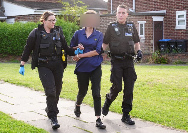 A woman with her faced blurred is lead in handcuffs by two police officers