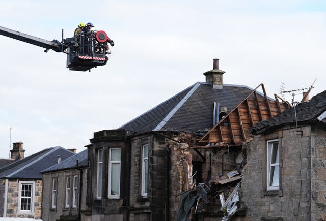 Firefighters on high cherry picker alongside building with damaged roof