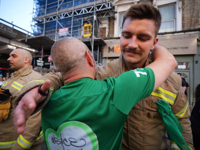 A person hugs a firefighter during a silent march in west London in memory of those killed in the Grenfell Tower disaster, on the eighth anniversary of the fire 