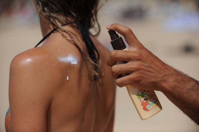 A man sprays sun cream on to the back of a woman wearing a bikini