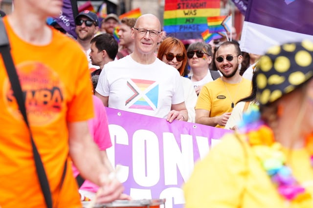 John Swinney wearing a Pride T-shirt and holding a banner with other marchers 