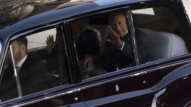 The King and the Queen Consort wave from the back of a car.