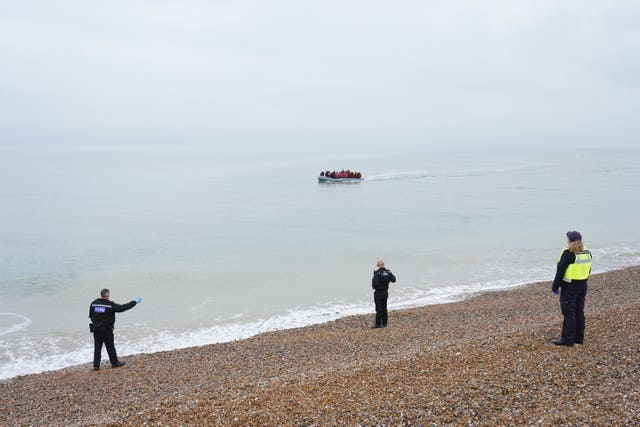Members of the police and Border Force watch as a dinghy carrying people thought to be migrants, arrives on a beach in Dungeness, Kent (Gareth Fuller/PA)