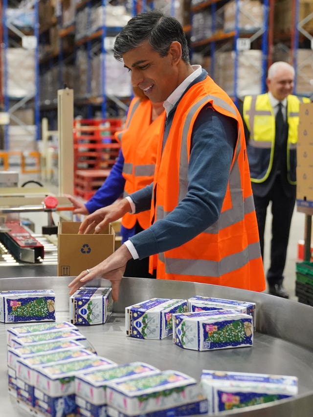 Rishi Sunak in a hi-vis packs products on an assembly line