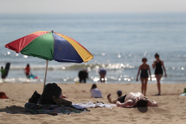 People lying and walking on a beach, with the sea in the background