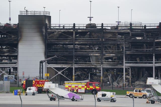 Burned out shells of cars, buried amid debris of a multi-storey car park, with emergency vehicles nearby