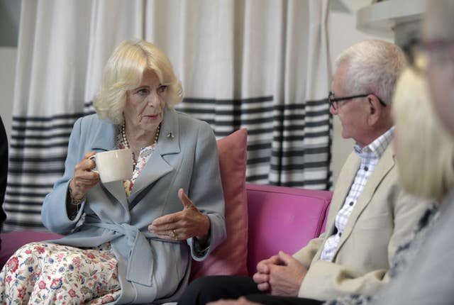 The Queen chatting to people while holding a mug