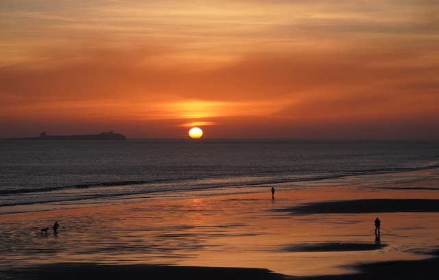 People during sunrise at Bamburgh Beach, looking out to the Farne Islands in Northumberland