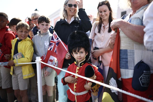 Members of the public, including a young boy dressed as a Royal Guardsman, waiting for the arrival of the King