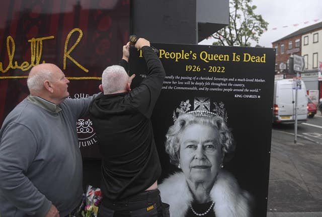 Council workers and local community representatives hang a mural on a wall in Crimea Street, off Shankill Road in Belfast following the Queen's death