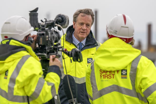 Alister Jack in a hi-vis jacket speaking while being interview on camera