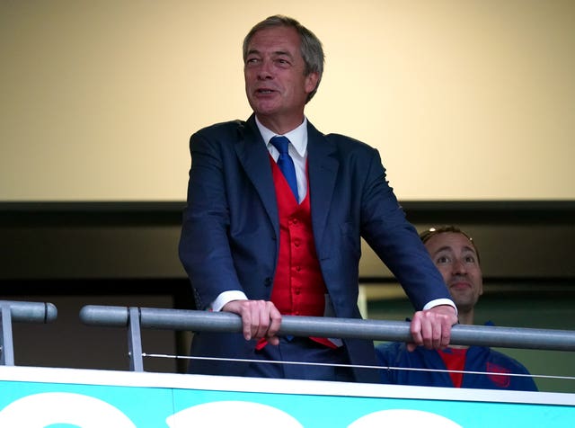 Nigel Farage wearing a blue suit with a red waistcoat places his hands on a rail