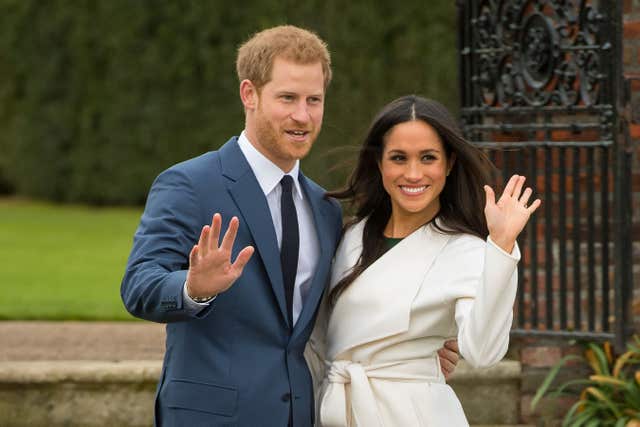 Harry and Meghan smile and wave at the cameras during their engagement announcement photocall