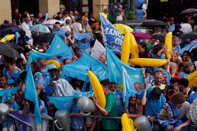 Manchester City fans take shelter from the rain ahead of the treble parade