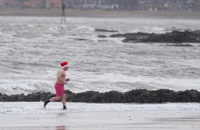 A man running in a Santa hat on  a beach