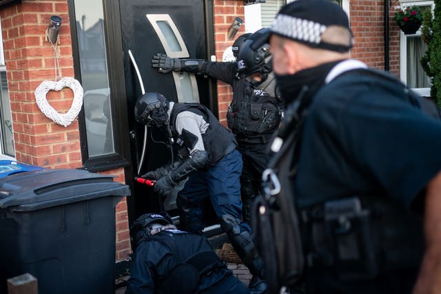 The backs of officers as they use a metal enforcer to smash open the front door.