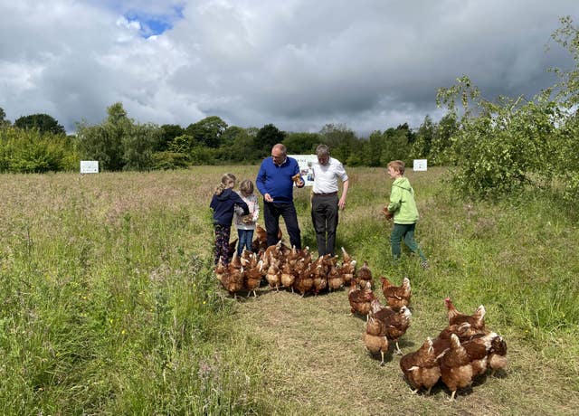 Sir Ed Davey and three children in a field with a flock of chickens