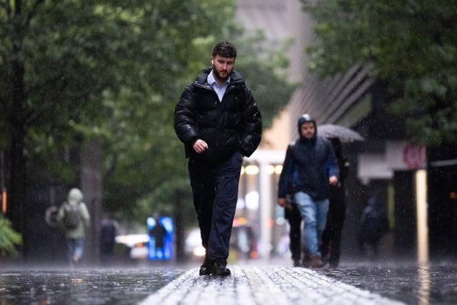 People wearing waterproof coats, hoods and carrying umbrellas walking in the rain in London