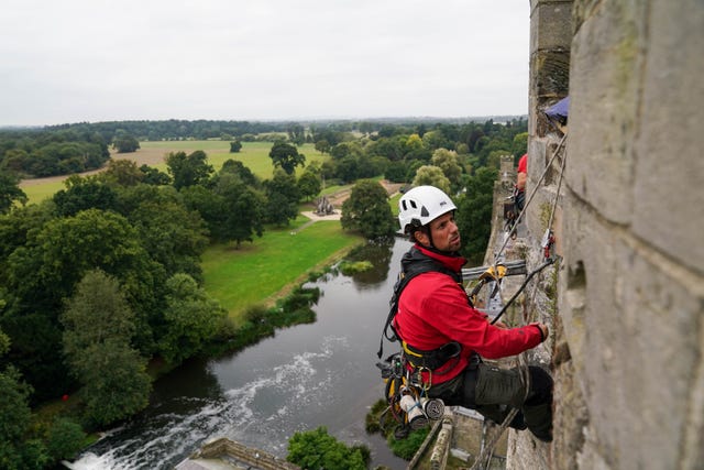 Restorer cleaning high up at Warwick Castle with river in the background