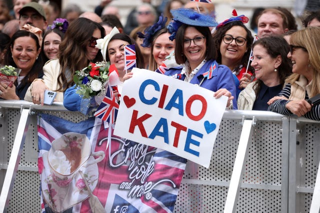 A woman holds a sign which says 'Ciao Kate'