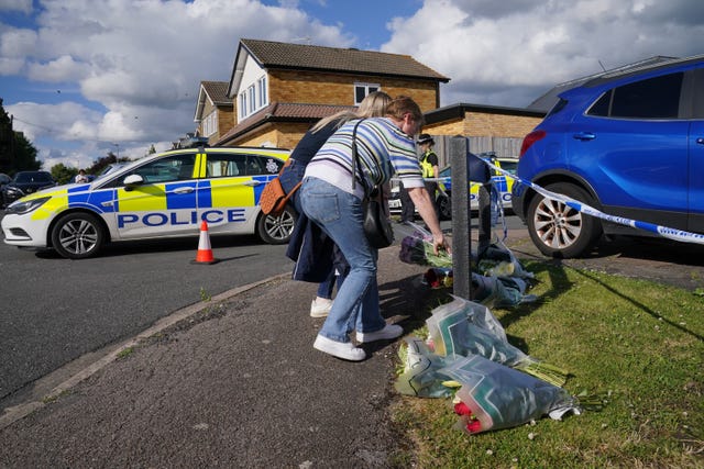 A man and woman deliver floral tributes near to the scene in Ashlyn Close, Bushey, Hertfordshire 