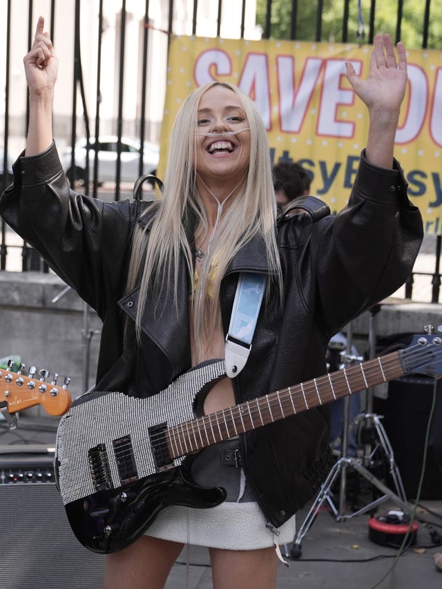 Ashleigh Harley raising her arms up smiling while a guitar rests in on her chest