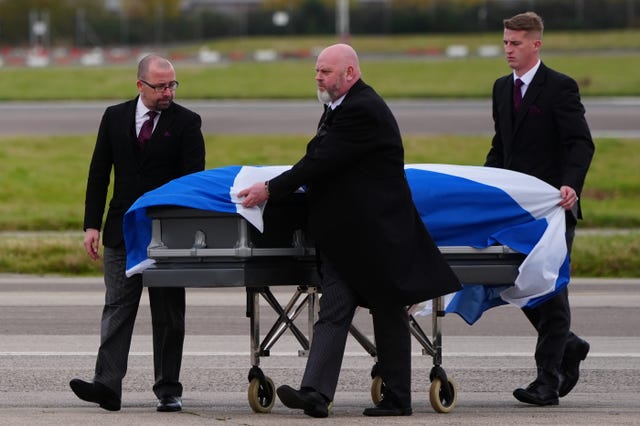 Alex Salmond's coffin, draped in Scottish flag, is moved on a trolley by three men in suits